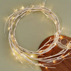 Couronne lumineuse LED décorative en branches blanches, posée sur une table verte avec un dessous de plat en rotin. Éclairage d'ambiance moderne.