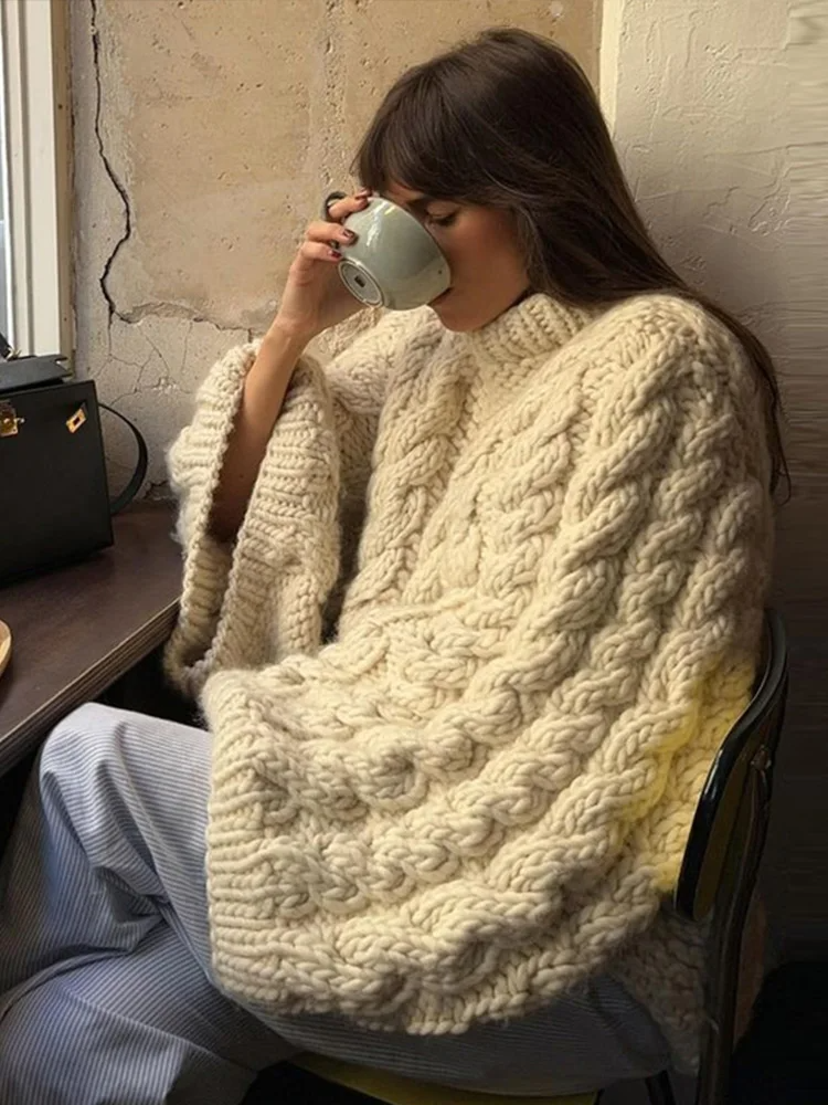 Femme buvant du café, portant un poncho en laine tricoté, assise près d'une fenêtre. Mode automne-hiver, confort, style décontracté.