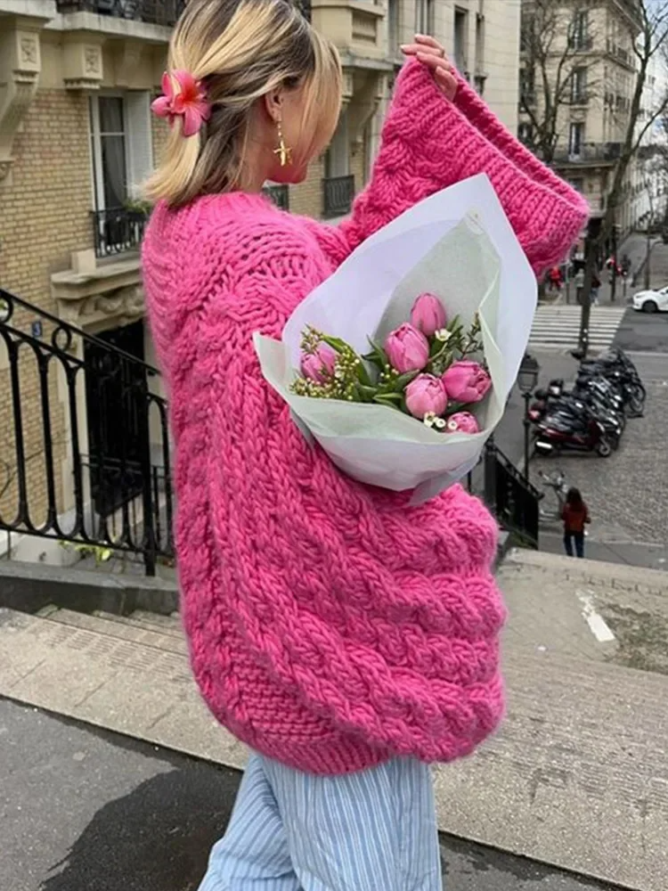 Femme en pull rose épais, tenant un bouquet de tulipes roses, marche en ville. Mode hiver, style urbain, fleurs fraîches, rue parisienne.
