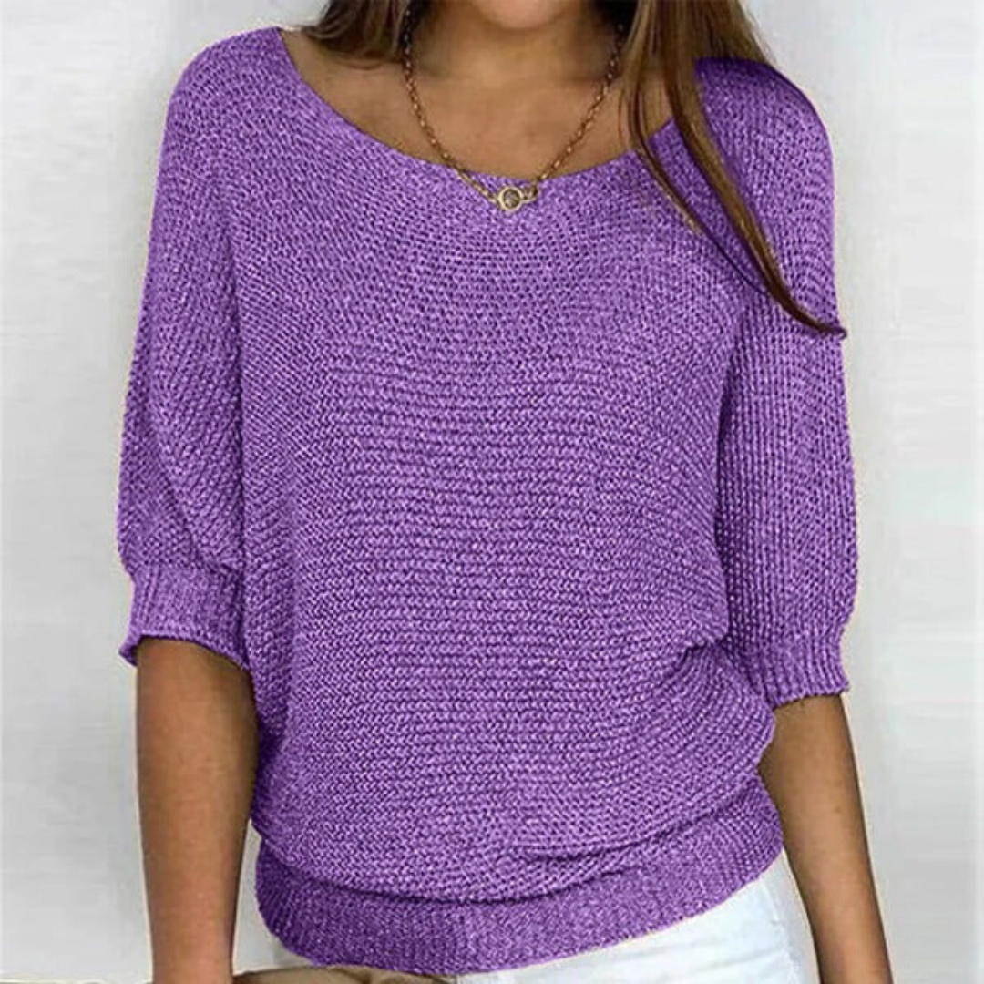 Femme portant un pull violet en tricot à manches trois-quarts, col bateau, avec un collier doré, sur fond blanc. Mode féminine élégante.