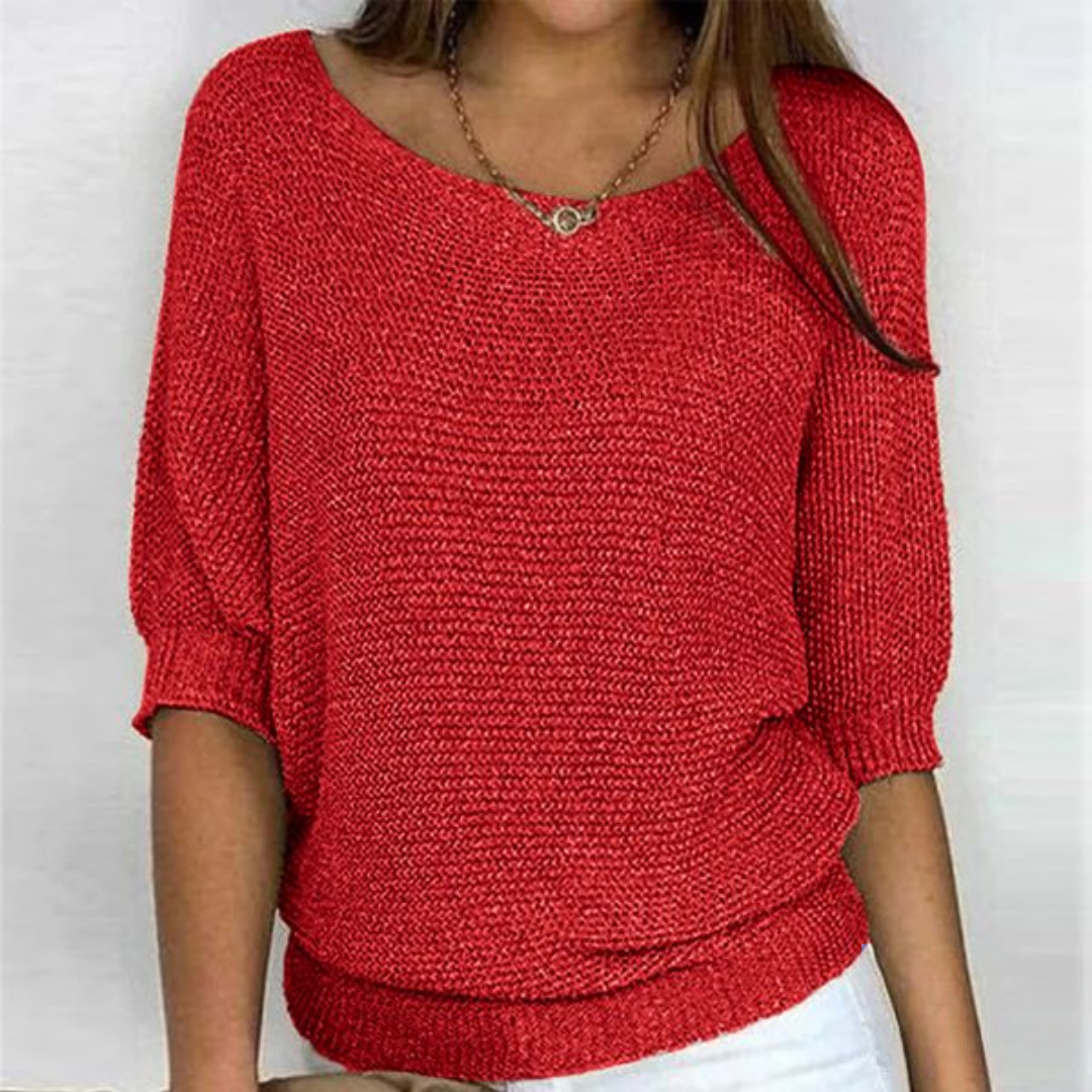 Femme portant un pull rouge en tricot, manches trois-quarts, col bateau, avec un collier doré. Mode féminine, tenue décontractée élégante.