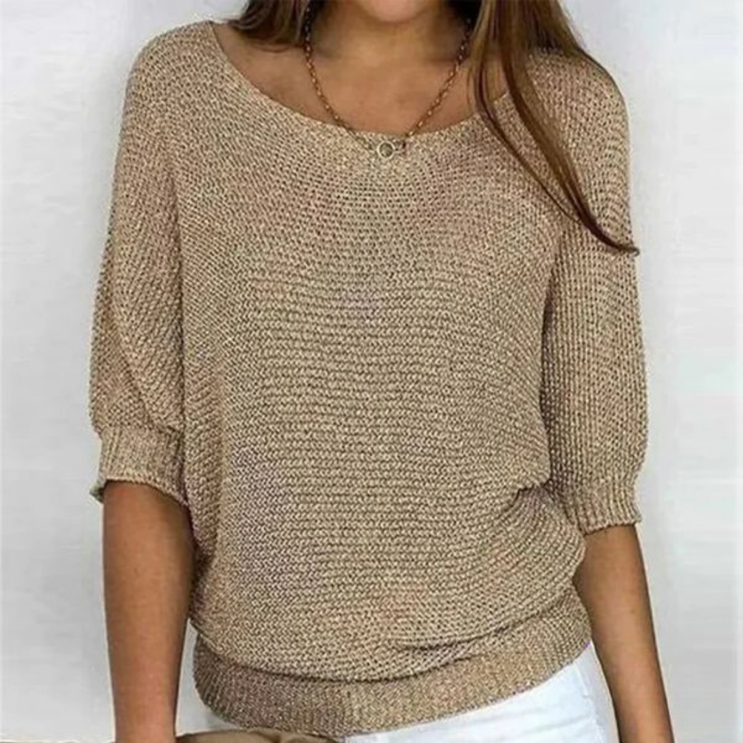 Femme portant un pull beige en tricot à manches courtes, col rond, avec un collier doré, sur fond blanc. Mode féminine, tenue décontractée.