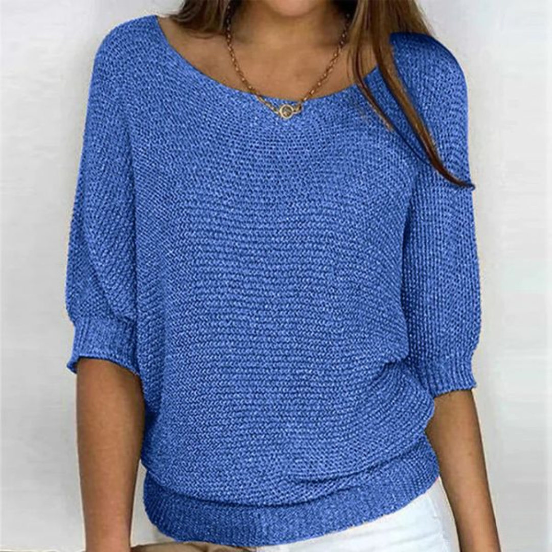 Femme portant un pull bleu en tricot, manches trois-quarts, col bateau, avec un collier doré. Mode féminine, tenue décontractée, style élégant.