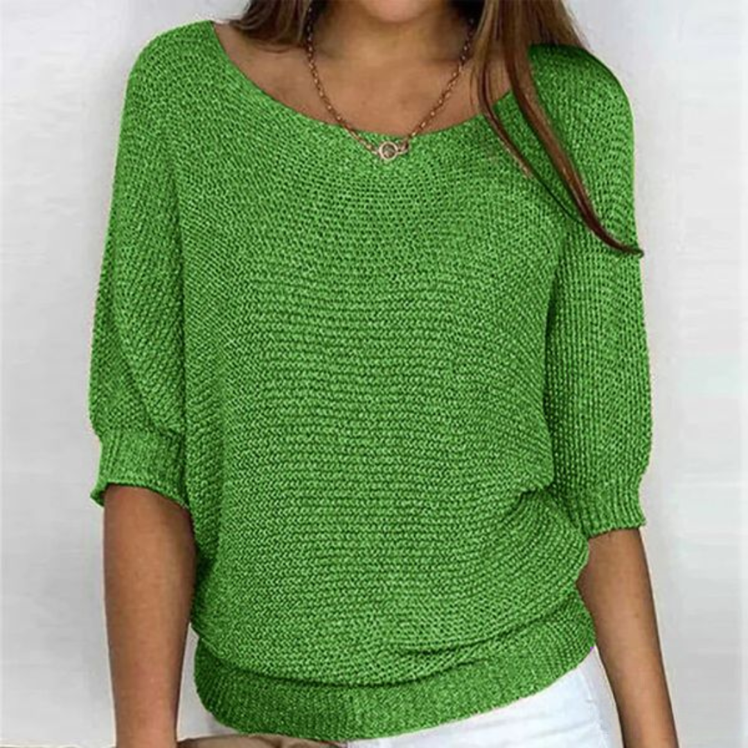 Femme portant un pull vert en tricot, manches trois-quarts, col bateau, avec un collier doré. Mode féminine, tenue décontractée, style moderne.