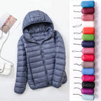 Veste matelassée grise avec capuche, accompagnée de sacs de rangement colorés. Mode hiver, vêtements chauds, veste légère et compressible.