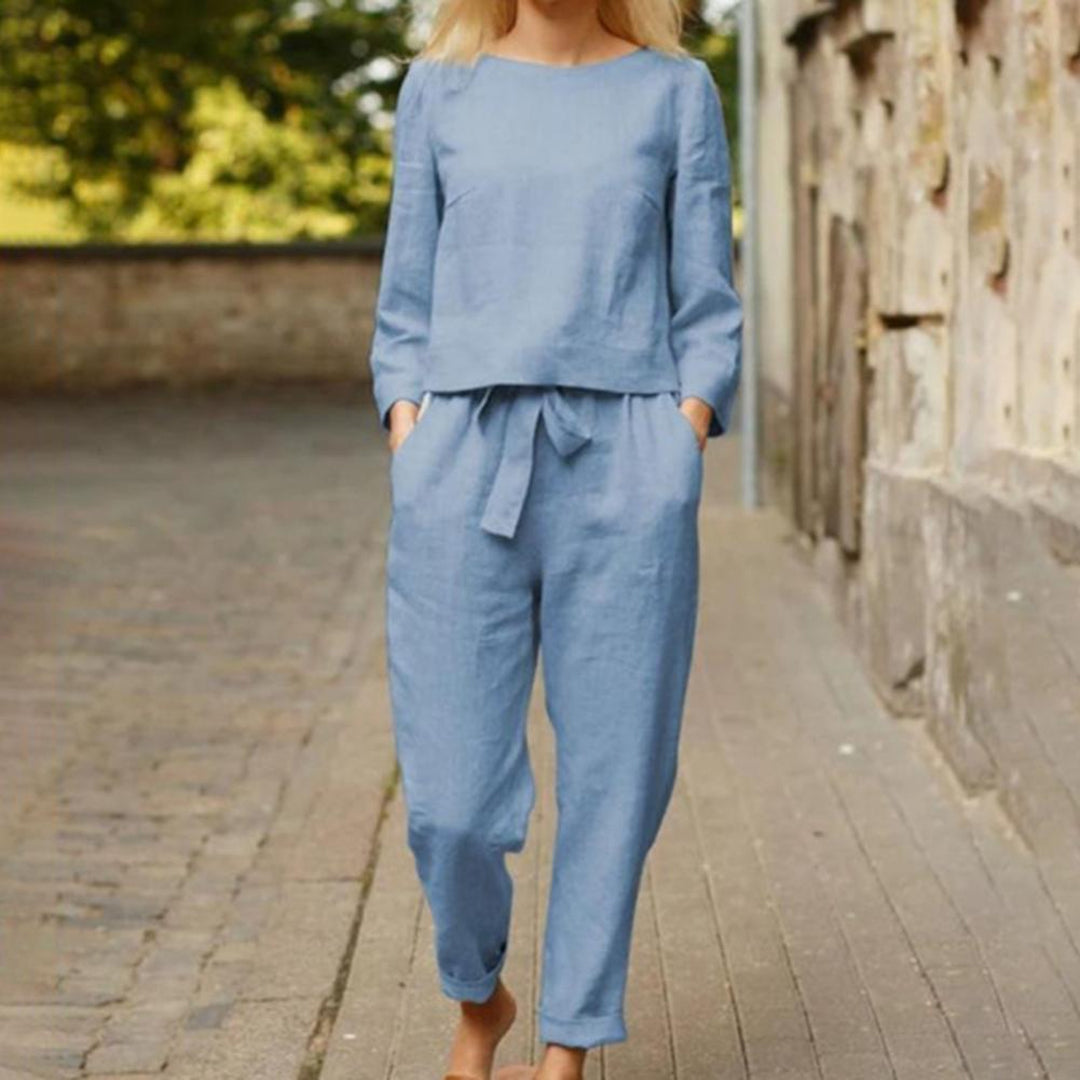 Femme portant un ensemble en lin bleu clair, composé d'un haut à manches longues et d'un pantalon ample, marchant sur une rue pavée.