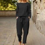 Femme portant un ensemble noir élégant, composé d'un haut à manches longues et d'un pantalon ample, marchant sur une rue pavée. Mode décontractée chic.