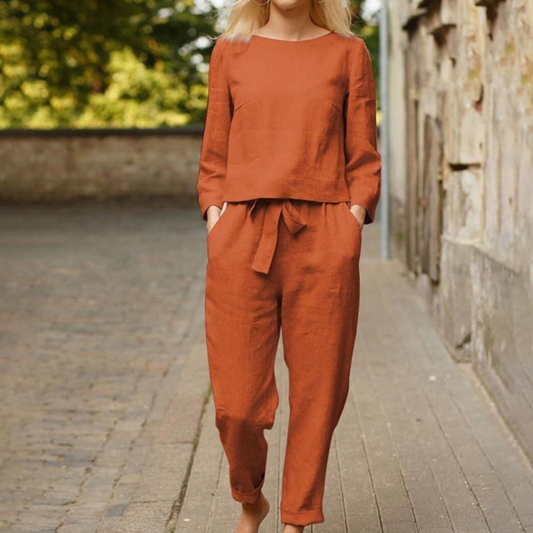 Femme portant un ensemble en lin orange, composé d'un haut à manches longues et d'un pantalon taille haute, sur une rue pavée. Mode automne chic.