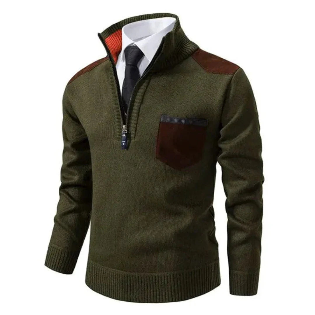 Pull-over vert à col zippé, avec poche poitrine marron et empiècements aux épaules, porté sur chemise blanche et cravate noire. Mode homme élégante.