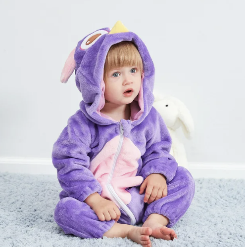 Enfant en pyjama violet à capuche hibou, assis sur un tapis bleu, avec un jouet lapin blanc en arrière-plan. Mode bébé, vêtements confortables.