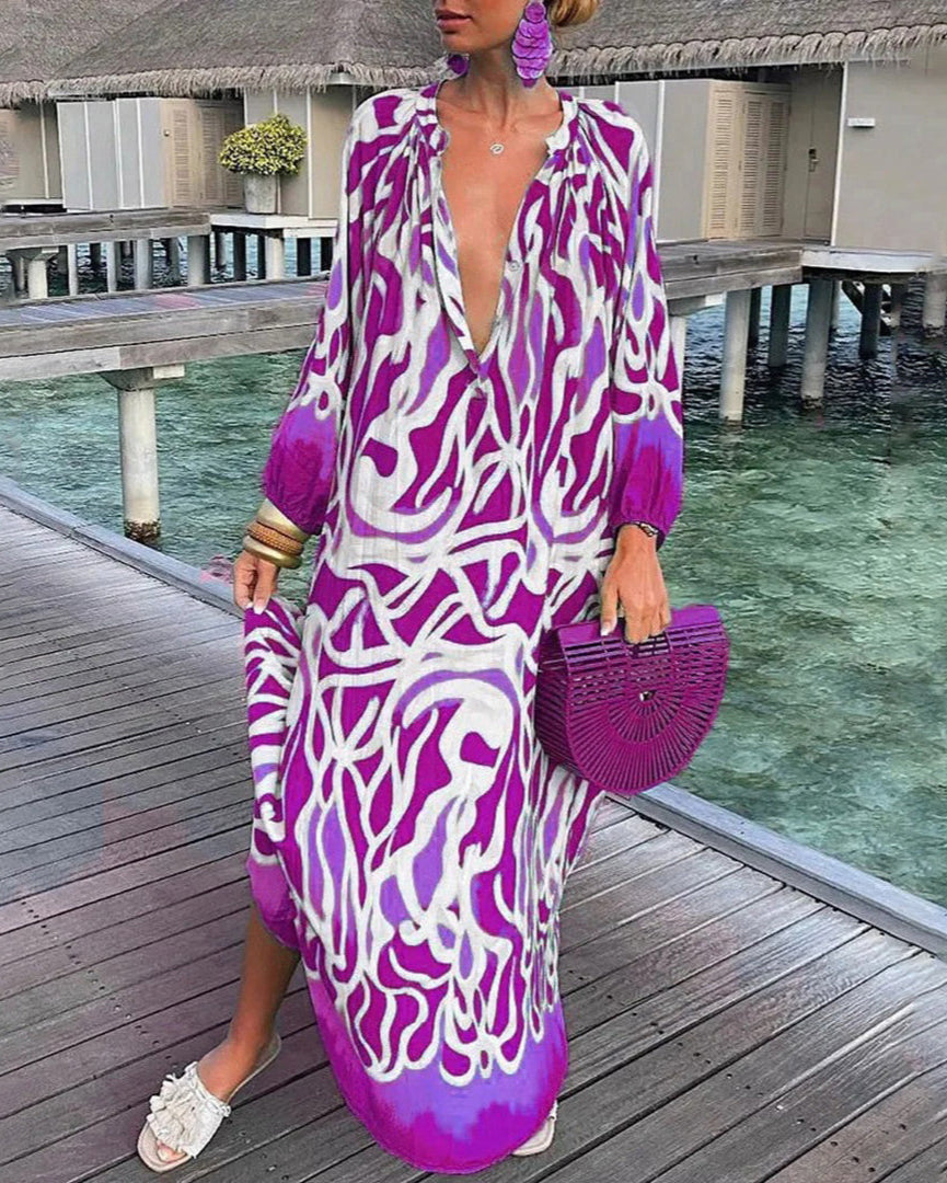 Robe longue violette et blanche à motifs abstraits, portée par une femme sur un ponton en bois, avec sac à main assorti et sandales blanches.