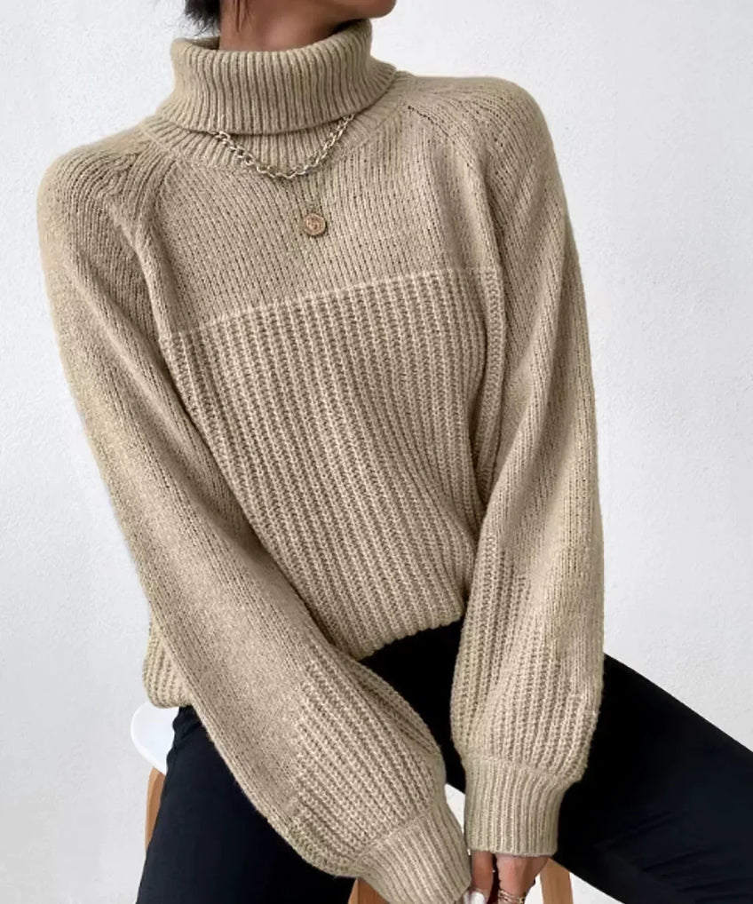 Pull en maille beige à col roulé, manches longues, porté avec un collier doré, sur fond blanc. Mode automne-hiver, style décontracté et élégant.