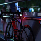 Vélo de route noir avec feux arrière LED rouges, garé sur un pont la nuit. Éclairage urbain, cyclisme nocturne, sécurité vélo.