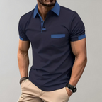 Homme portant un polo bleu marine élégant avec col contrastant, manches courtes, poche poitrine, associé à un pantalon beige. Mode masculine décontractée.