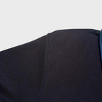 Épaule de veste noire en tissu texturé, couture visible, fond blanc. Mode masculine, vêtement élégant, détail couture veste.