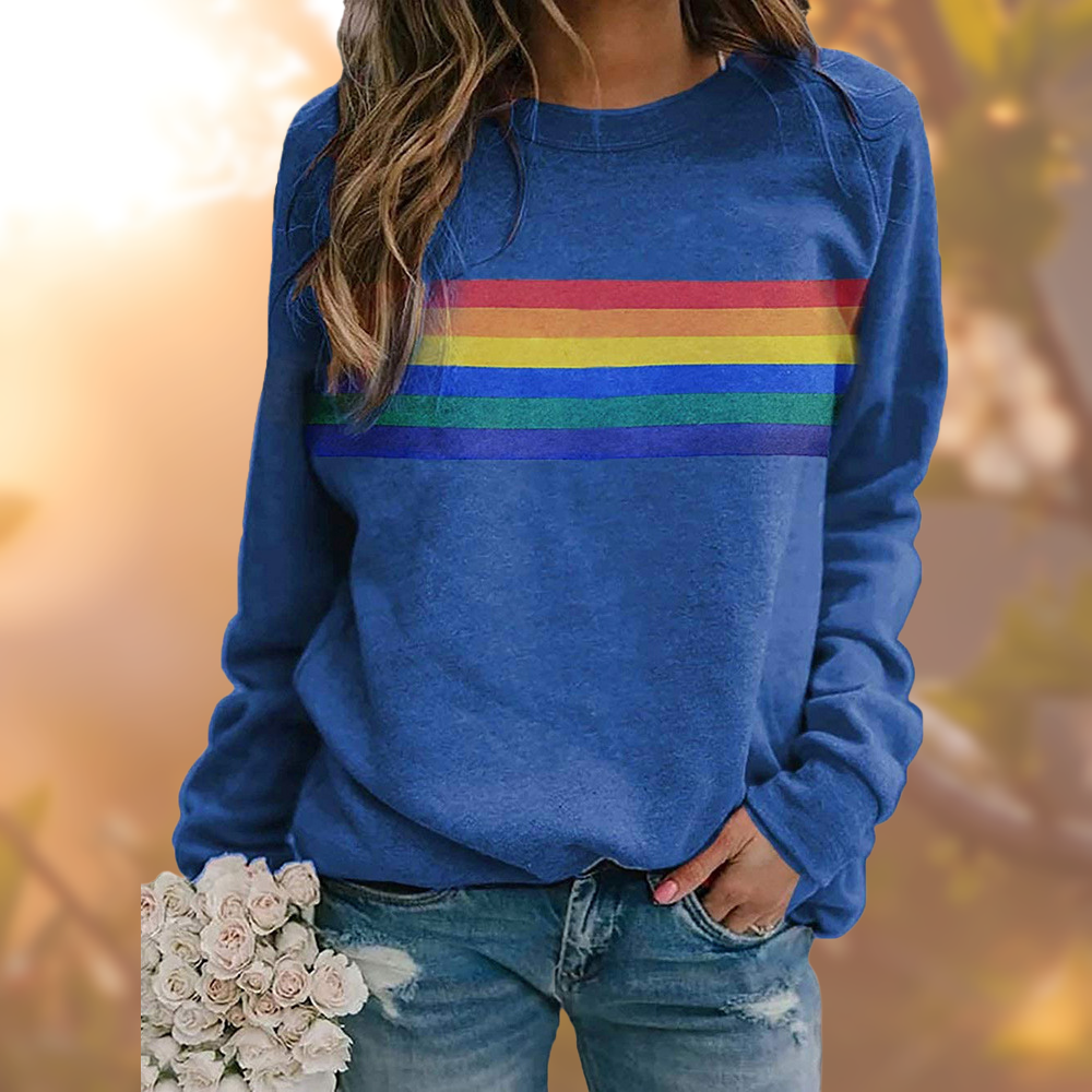 Femme portant un sweat bleu avec rayures arc-en-ciel, tenant un bouquet de roses blanches. Mode décontractée, style coloré, tendance automne.
