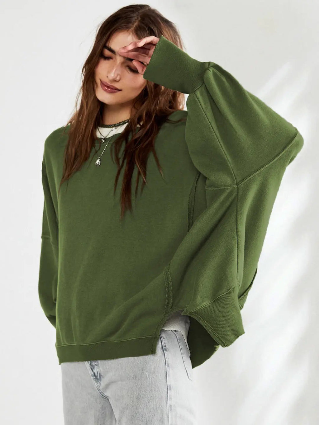 Femme portant un pull vert ample, manches larges, avec un jean clair. Mode décontractée, tendance automne, style confortable et moderne.