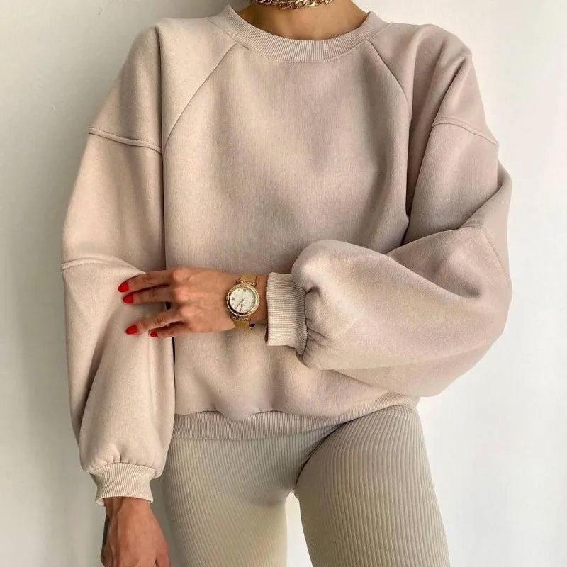 Femme portant un pull beige ample et un pantalon côtelé, montre dorée au poignet, pose élégante. Mode décontractée, tendance automne-hiver.