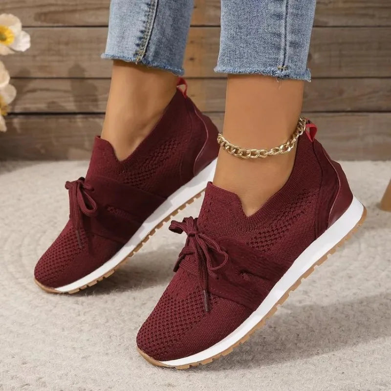 Chaussures de sport bordeaux pour femme, en maille respirante, avec lacets et semelle blanche, portées avec un jean. Mode décontractée tendance.