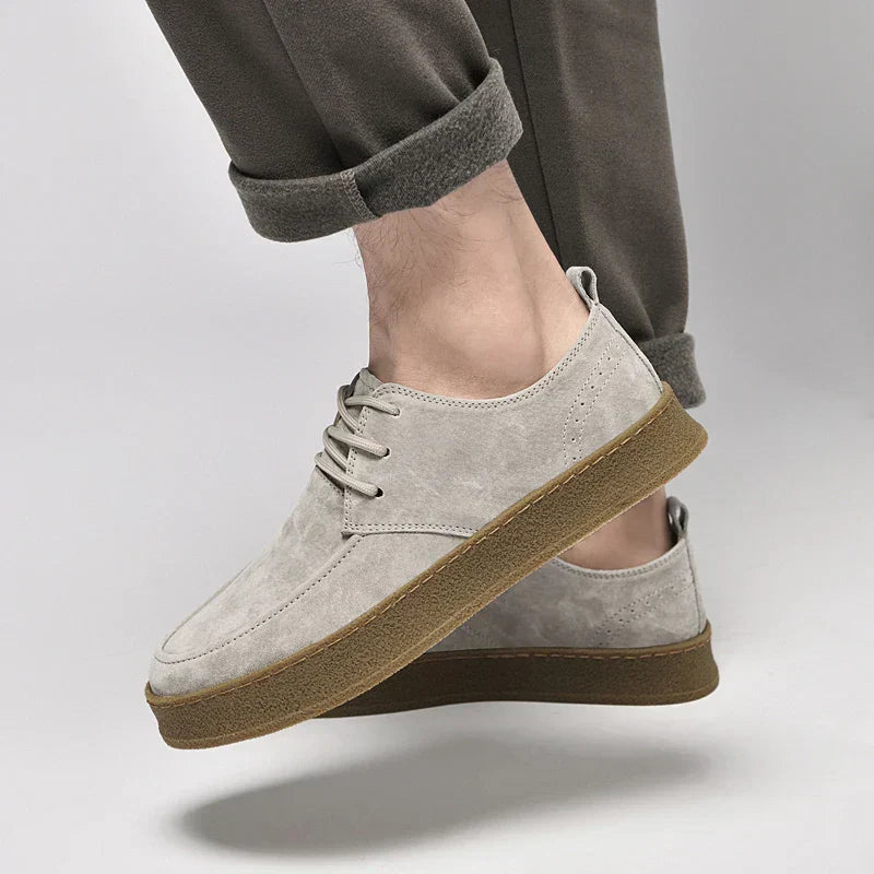 Chaussures en daim gris clair pour homme avec semelle marron, style décontracté, portées avec un pantalon retroussé. Mode masculine élégante.