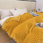 Lit avec couverture en peluche jaune texturée, oreillers blancs, plateau avec tasse et magazine. Décor de chambre moderne et confortable.