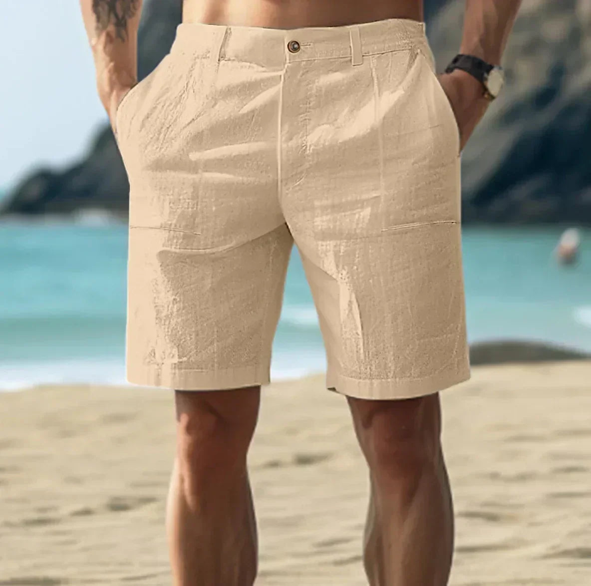 Short beige en lin pour homme sur une plage ensoleillée, mer et montagnes en arrière-plan. Mode estivale, tenue décontractée, vacances bord de mer.