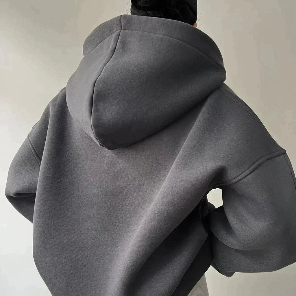 Personne portant un sweat à capuche gris foncé, dos tourné, style décontracté. Mode automne-hiver, vêtement chaud et confortable.