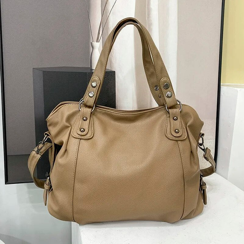 Sac à main en cuir beige élégant avec poignées renforcées et détails métalliques, posé sur une surface moderne. Accessoire mode femme chic et tendance.