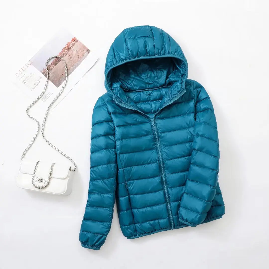 Veste doudoune bleue avec capuche sur fond blanc, accompagnée d'un sac à main blanc élégant. Mode hiver, vêtement chaud et tendance.