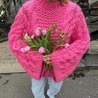 Femme en pull rose épais tenant un bouquet de tulipes roses et de muguet, debout sur un trottoir urbain. Mode hiver, fleurs fraîches.