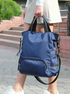 Sac à dos bleu porté par une personne en jupe blanche, avec des baskets blanches, sur un trottoir pavé. Accessoire mode pratique et tendance.