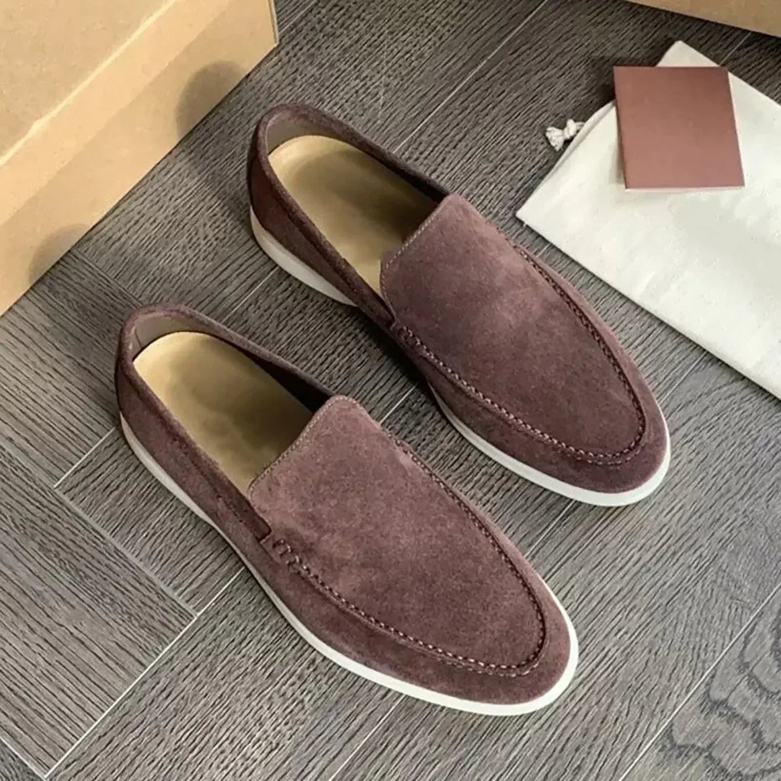 Mocassins en daim marron pour homme sur parquet gris, avec semelle blanche. Chaussures élégantes, confortables, idéales pour un style décontracté.