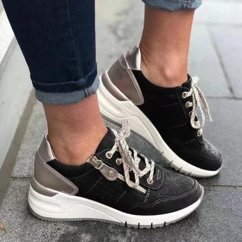 Chaussures de sport noires et blanches pour femme, avec lacets blancs et détails argentés, portées avec un jean. Mode urbaine tendance.