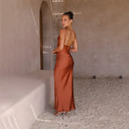 Robe longue dos nu en satin marron, femme élégante posant dans un décor minimaliste, lumière naturelle, mode chic et sophistiquée.