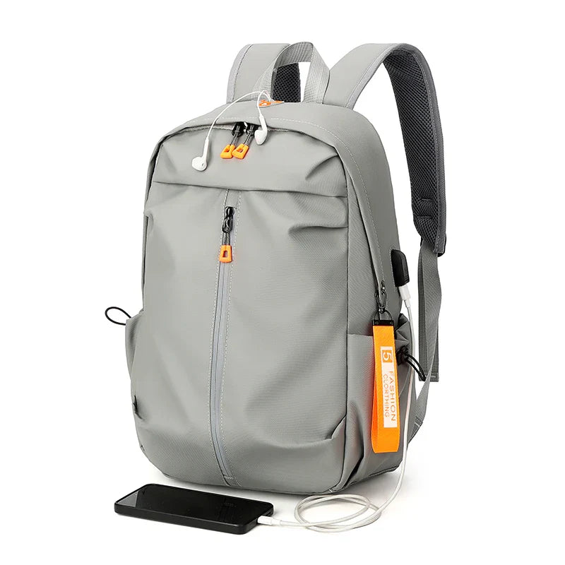 Sac à dos gris moderne avec port USB intégré, écouteurs blancs et étiquette orange, idéal pour étudiants et voyageurs. Accessoire pratique et tendance.