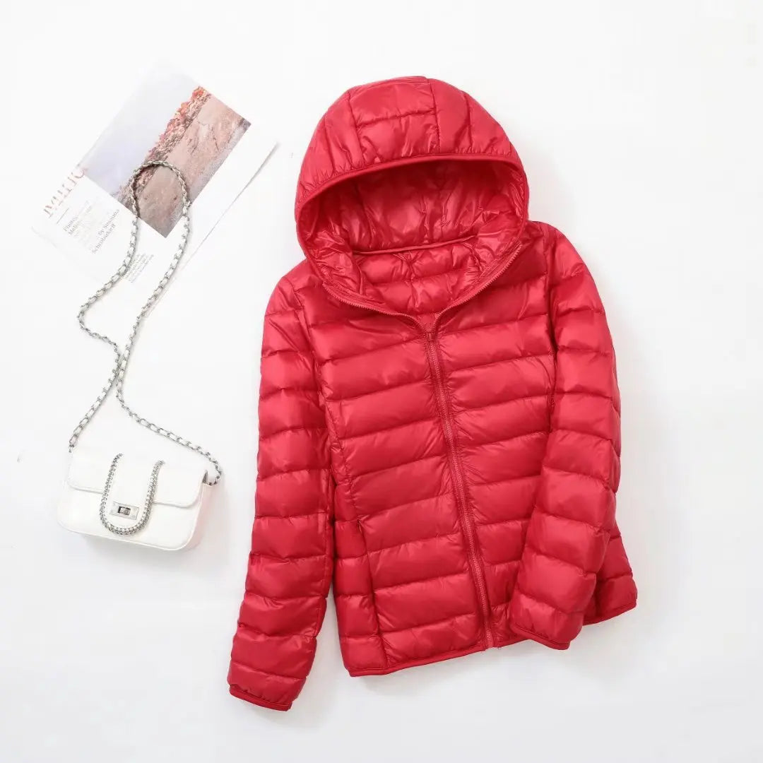 Veste doudoune rouge avec capuche sur fond blanc, accompagnée d'un sac à main blanc à chaîne argentée. Mode hiver, vêtement chaud.