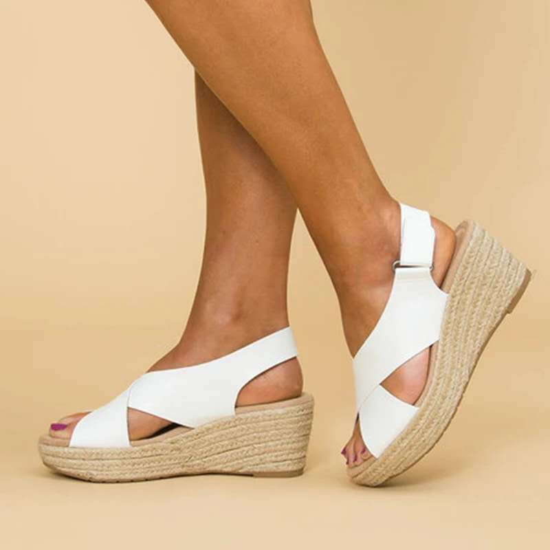 Sandales compensées blanches en cuir avec semelle en corde, portées sur fond beige. Chaussures d'été élégantes pour femmes, mode tendance.