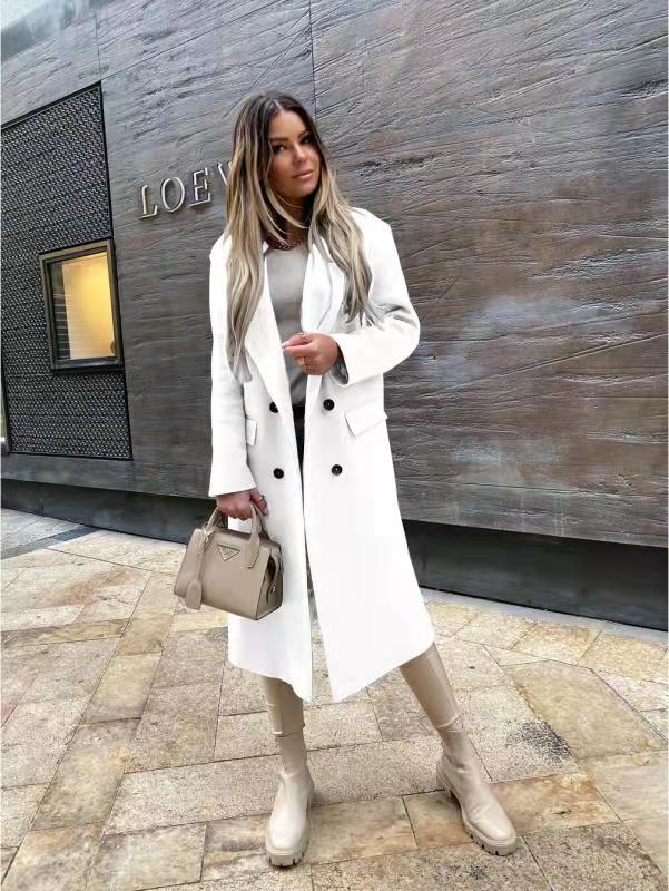 Femme portant un manteau blanc élégant, bottes beiges et sac à main Prada, posant devant un mur texturé avec le logo Loewe. Mode automne chic.