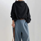 Personne portant un pull noir ample et un pantalon bleu taille haute, accessoirisé d'une ceinture marron et d'un sac à main. Mode décontractée élégante.