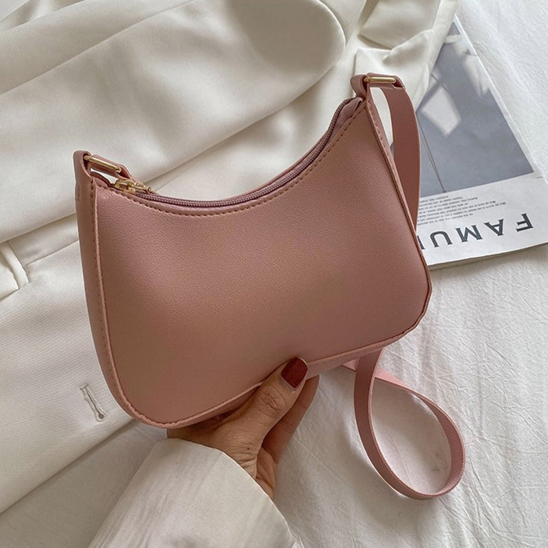Sac à main rose pastel élégant sur fond de tissu blanc, avec une fermeture éclair dorée et une bandoulière, idéal pour la mode féminine tendance.