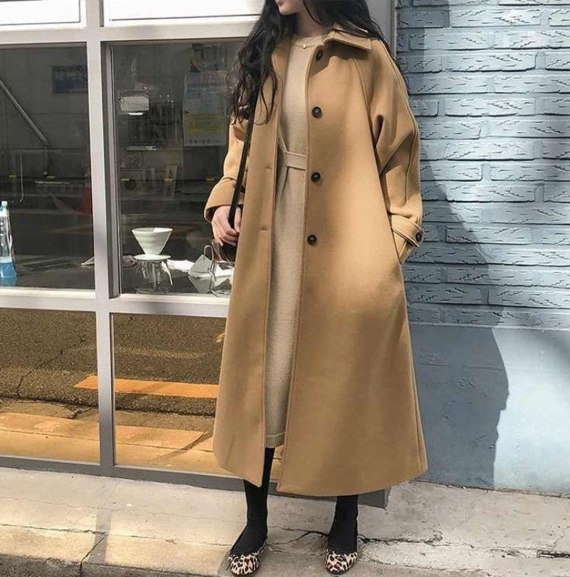 Femme portant un manteau long camel, robe beige, chaussures léopard, devant une vitrine. Mode automne-hiver, style élégant et moderne.