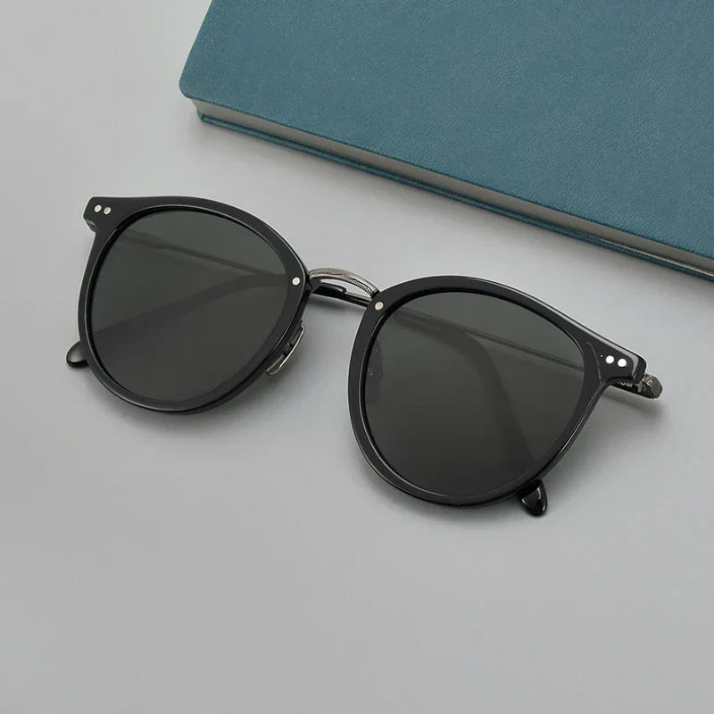 Lunettes de soleil noires élégantes posées sur une surface grise avec un livre bleu en arrière-plan. Accessoire mode tendance et chic.