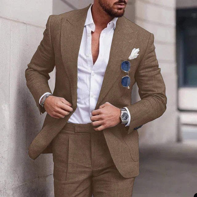 Homme élégant en costume marron, chemise blanche ouverte, lunettes de soleil accrochées, montre argentée, style mode masculine chic et moderne.