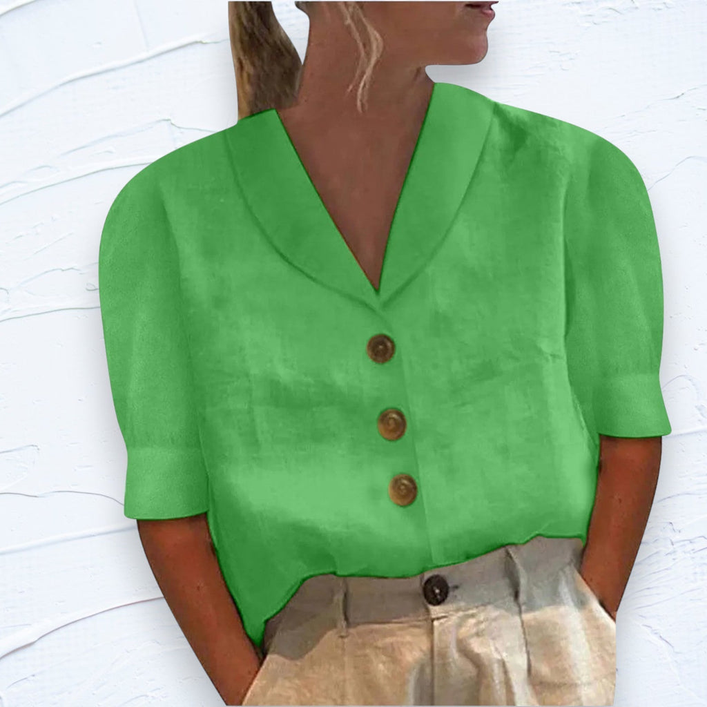 Femme portant une chemise verte à manches courtes avec boutons marron, associée à un pantalon beige. Mode estivale élégante et décontractée.
