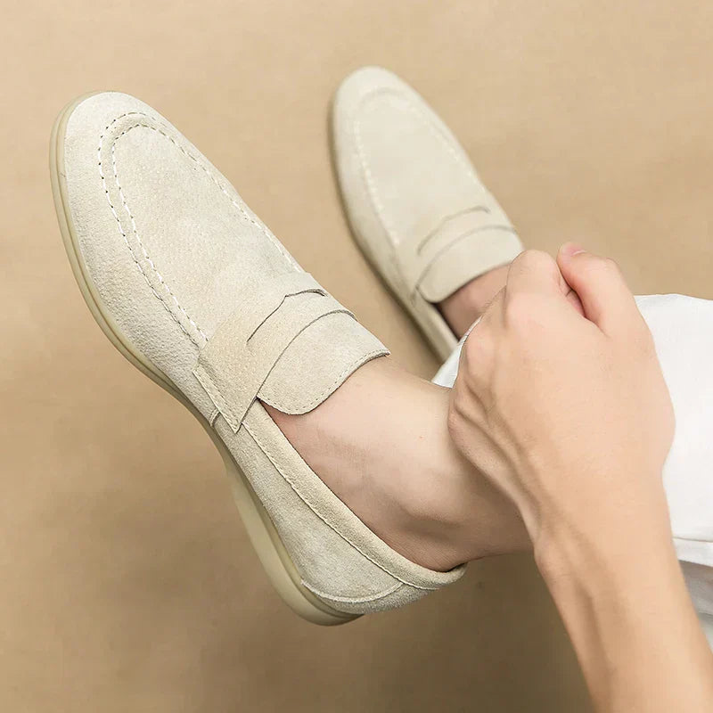 Chaussures mocassins en daim beige pour homme, élégantes et confortables, portées avec un pantalon blanc. Mode masculine, style décontracté.