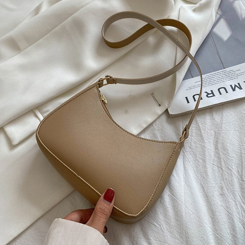 Sac à main beige élégant sur fond de tissu blanc, avec une main tenant la lanière. Accessoire mode tendance, style minimaliste et chic.