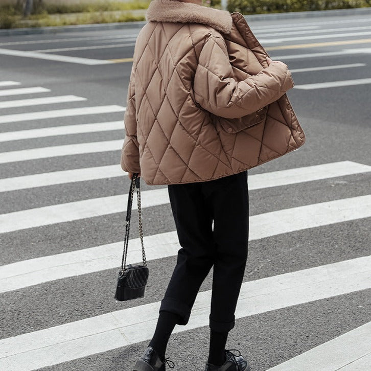 Personne portant une veste matelassée marron sur un passage piéton, tenant un petit sac à main noir. Mode automne-hiver, style urbain chic.