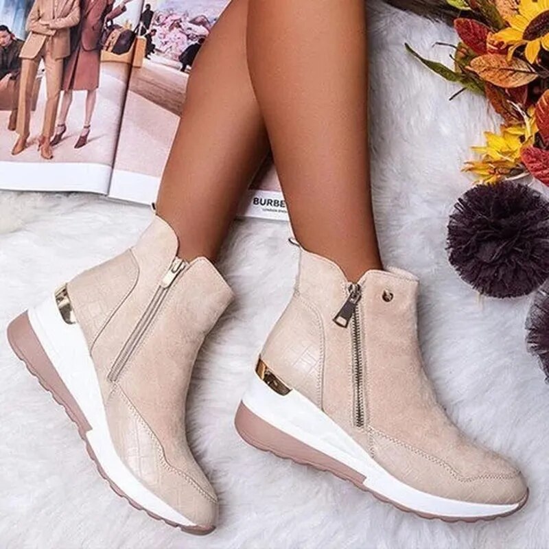 Bottes beige en daim avec fermeture éclair, semelle compensée blanche et détails dorés, posées sur un tapis blanc avec magazine et décor automnal.