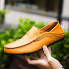 Chaussure mocassin en cuir marron clair pour homme, tenue en main, avec couture apparente, semelle noire, style décontracté et élégant.