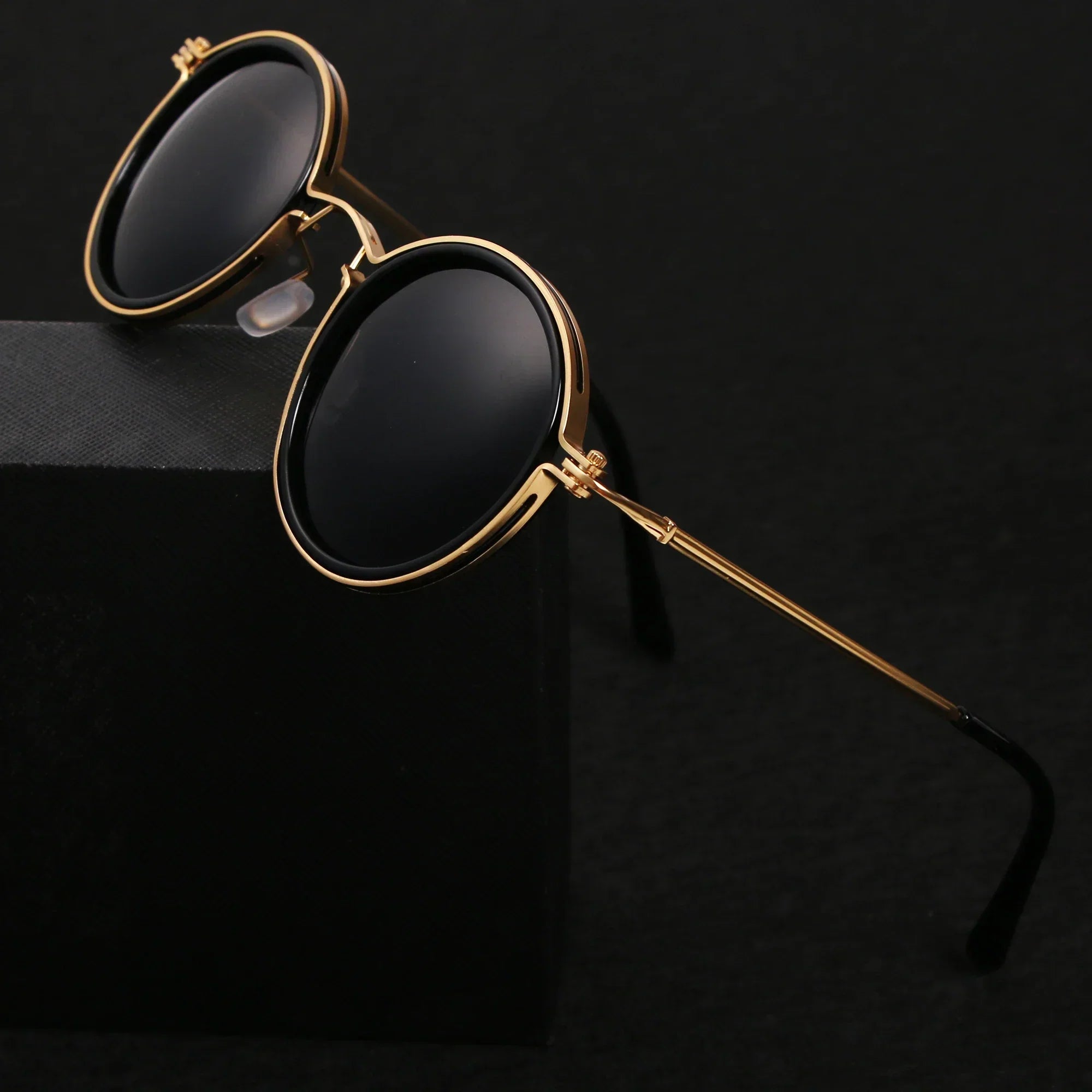 Lunettes de soleil rondes vintage avec monture dorée et verres noirs, posées sur fond noir. Accessoire mode élégant et tendance.